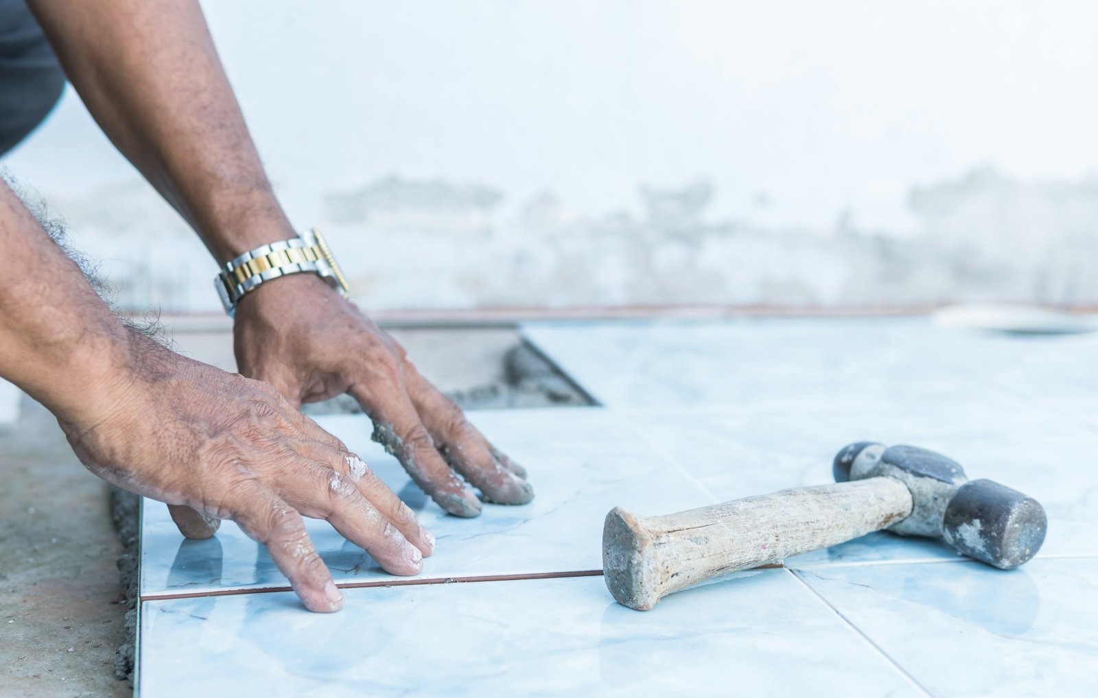 Hand worker flooring ceramic tile and hammer